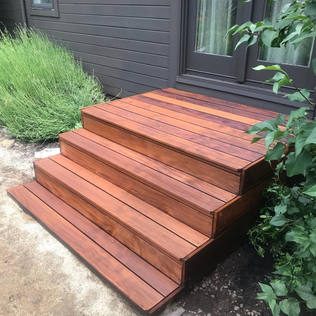 Wooden outdoor steps by dark house siding.