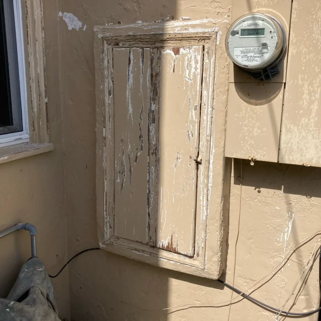 Peeling paint on exterior wall near electrical meter.