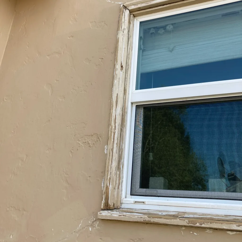 Weathered window frame on beige stucco wall.