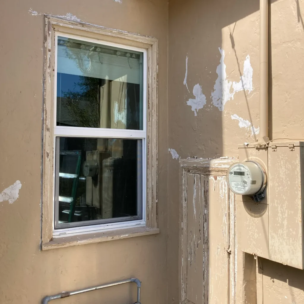 Peeling paint on building exterior with window and utility meter.