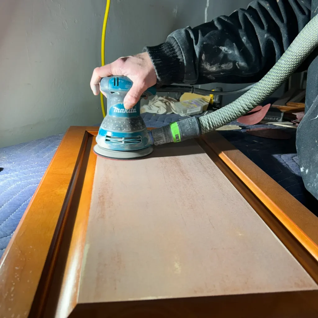 Person sanding wooden door with electric sander.