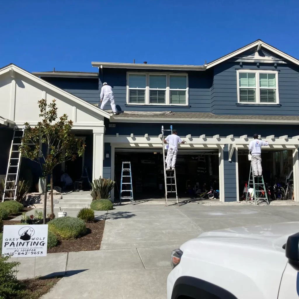 Painters working on exterior of blue two-story house facade.