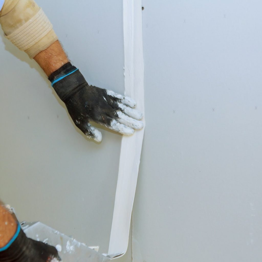 Worker applying caulk to drywall corner.